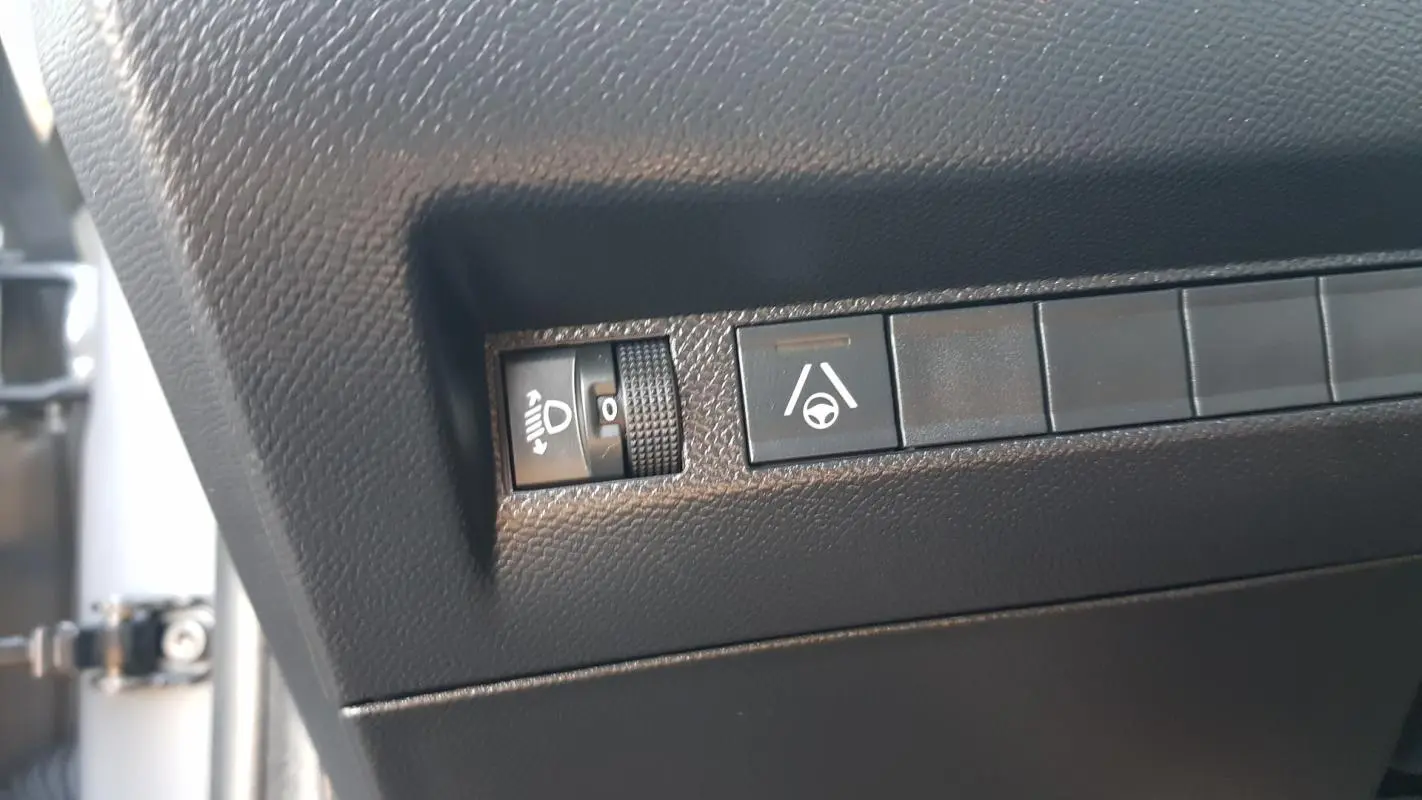 Gros plan sur les commandes de réglage des phares et d’aide à la conduite dans l’habitacle noir d’une Peugeot 208 gris 2024.