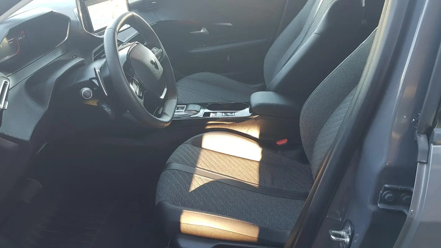 Vue intérieure côté conducteur de la Peugeot 208 Hybrid gris 2024, avec sièges tissu et volant multifonction.