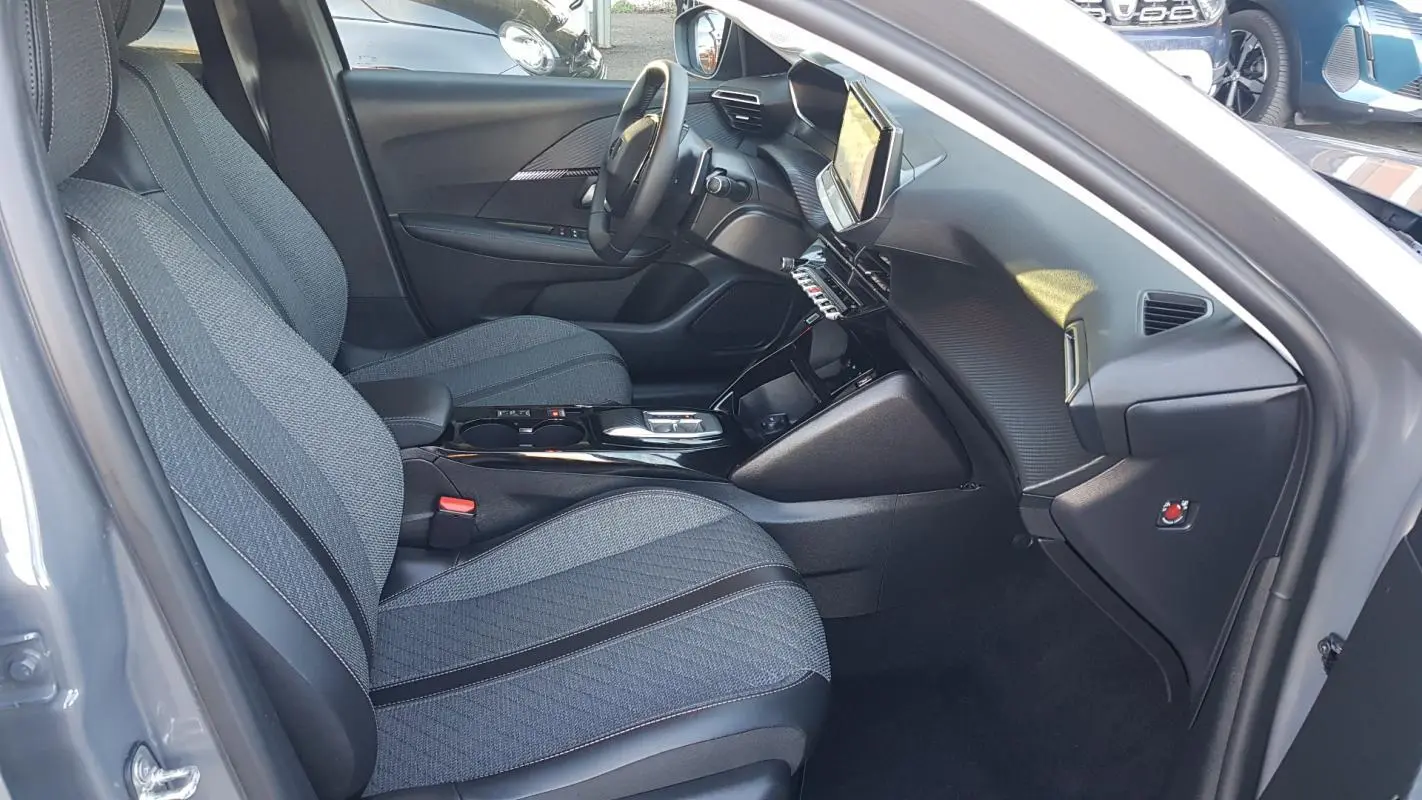 Vue intérieure côté conducteur de la Peugeot 208 Hybrid gris 2024, avec sièges tissu et écran tactile central.