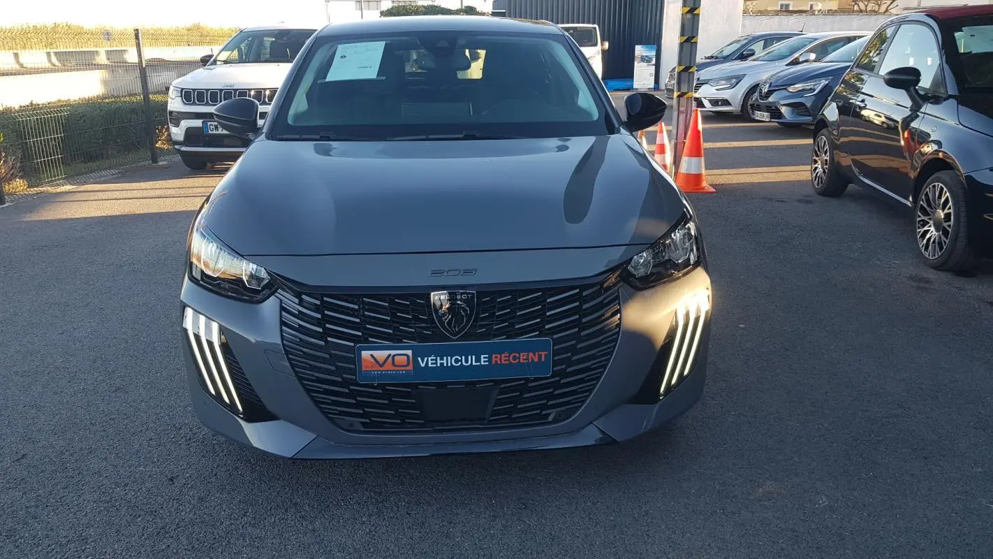 Vue de face d'une Peugeot 208 gris métallisé 2024 avec feux diurnes LED en forme de griffes et calandre noire distinctive.