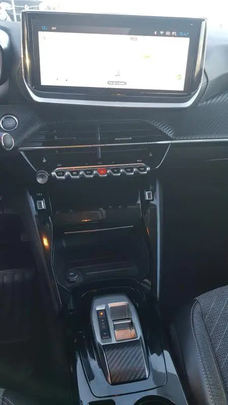 Vue rapprochée du tableau de bord et console centrale noire du Peugeot 208 Hybrid 100 e-DCS6 Allure 2024 avec écran tactile et levier de boîte auto.