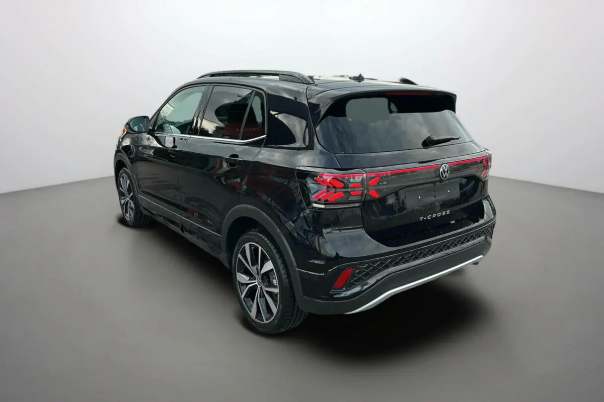 Vue 3/4 arrière droite du Volkswagen T-Cross noir intense avec jantes alu 18 pouces et barres de toit visibles.