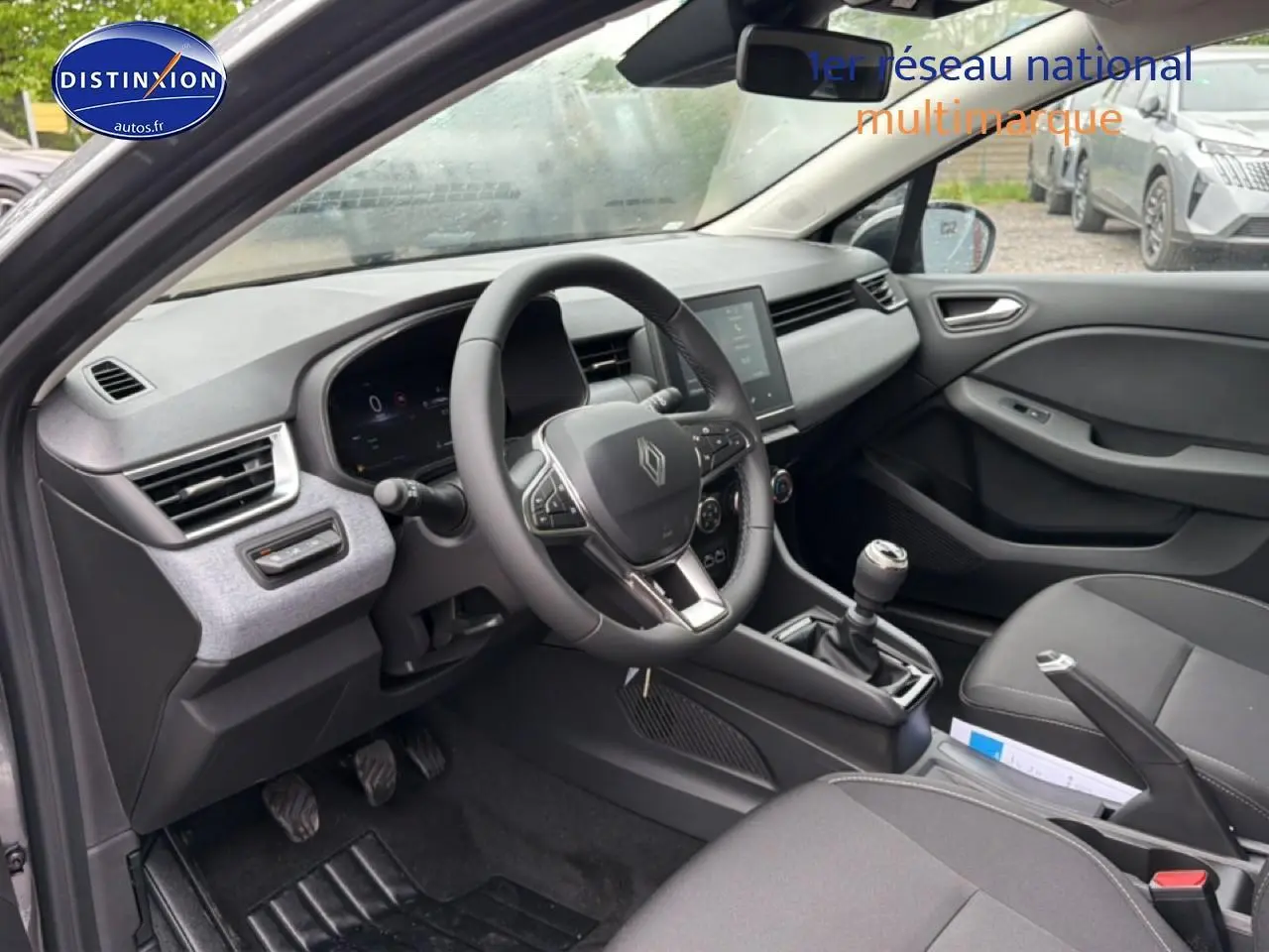 Vue intérieure côté conducteur de la Renault Clio V 1.0 TCe 90 gris schiste avec volant multifonction et boîte manuelle.