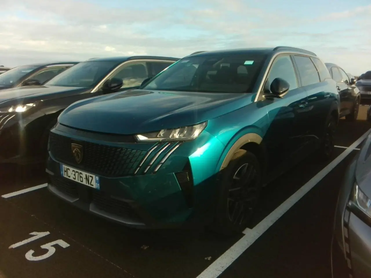 Peugeot 5008 bleu foncé vue 3/4 avant droit sur parking, calandre noire avec griffes LED distinctives.