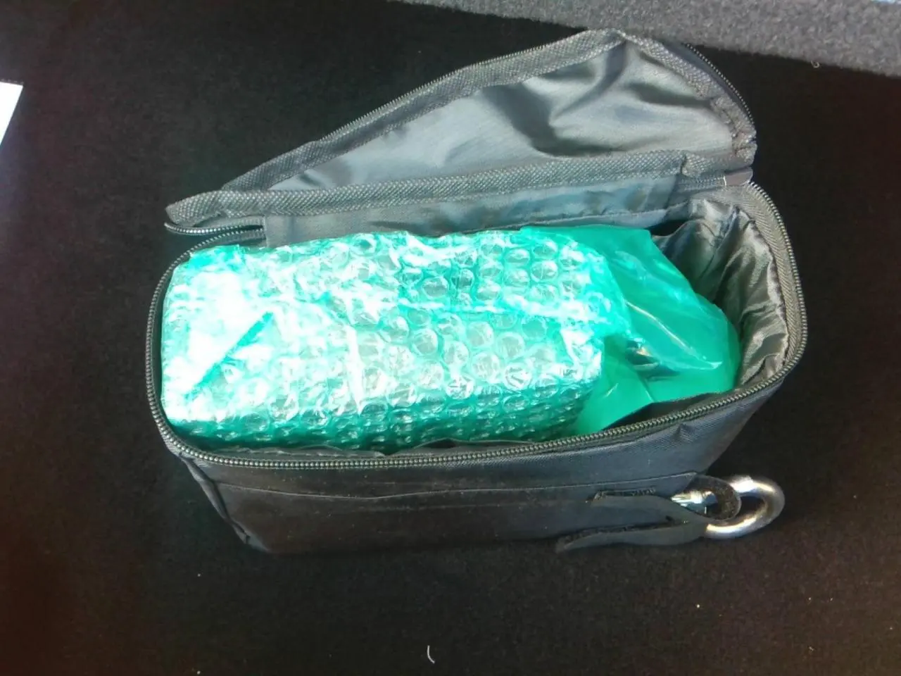 Intérieur du coffre avec sac noir ouvert contenant un objet emballé dans un film à bulles bleu-vert.