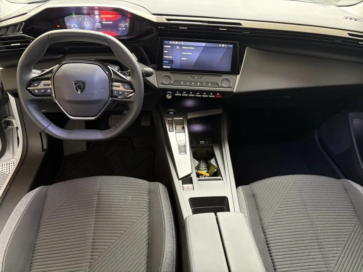 Vue intérieure avant de la Peugeot 308 blanche 2024, montrant le volant cuir multifonctions et l’écran tactile central.
