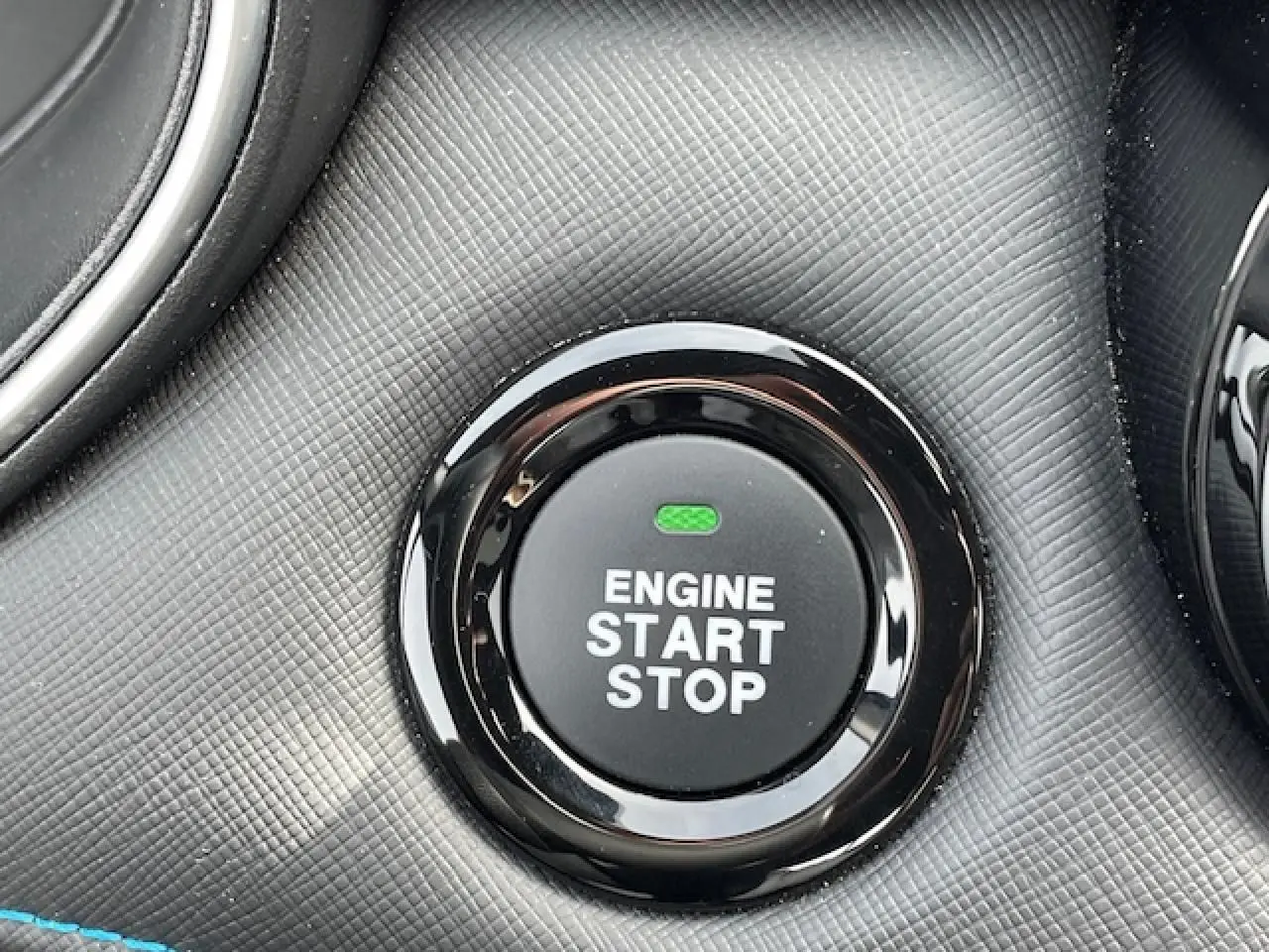 Gros plan sur le bouton noir brillant "Engine Start Stop" entouré d'une surface texturée gris foncé du tableau de bord.
