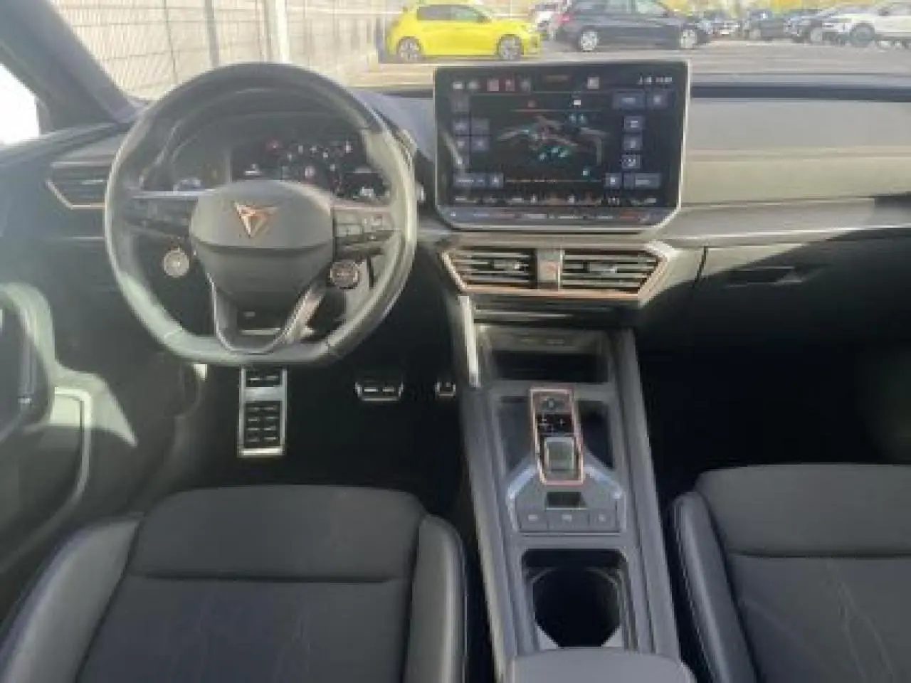 Vue intérieure avant de la CUPRA Leon 2025, volant cuir, écran tactile HD et console centrale moderne en noir.