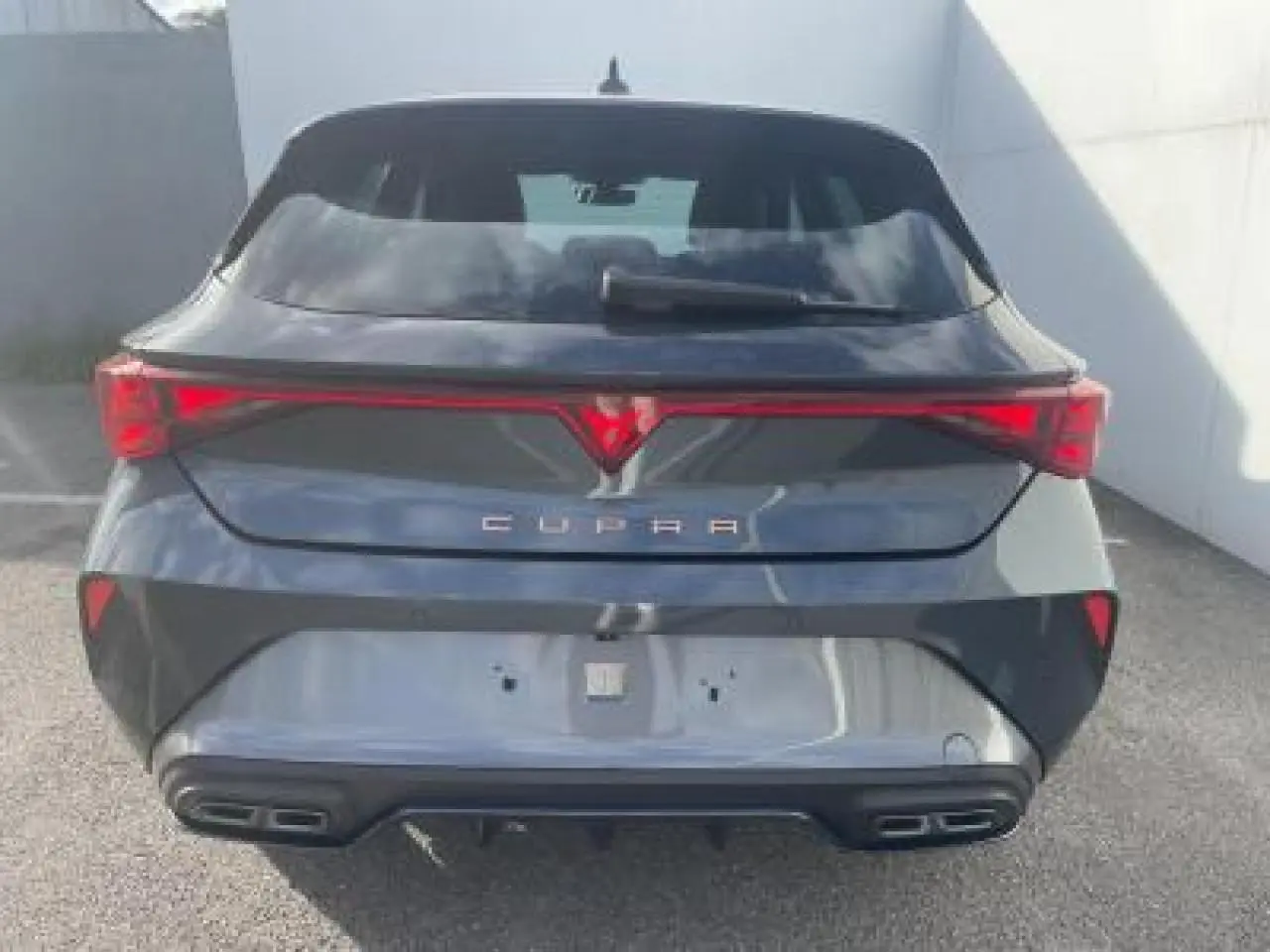 Vue arrière d'une CUPRA Leon 2025 gris magnetic metal avec bandeau lumineux et double sortie d'échappement noire stylisée.