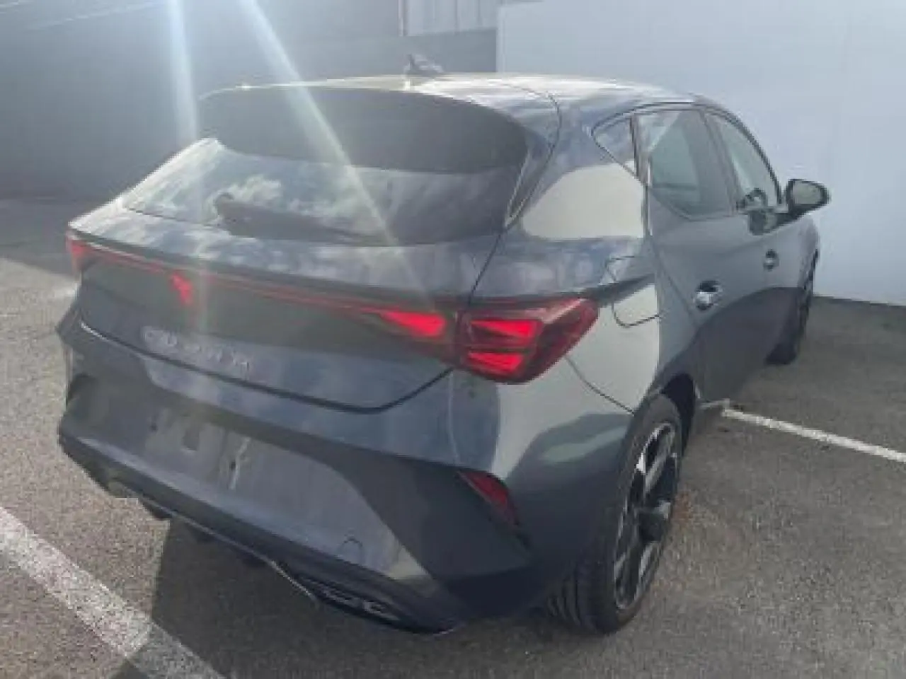 Vue 3/4 arrière droite d'une CUPRA Leon 2025 gris magnetic metal avec feux arrière Tri-LED et double sortie d'échappement noire.