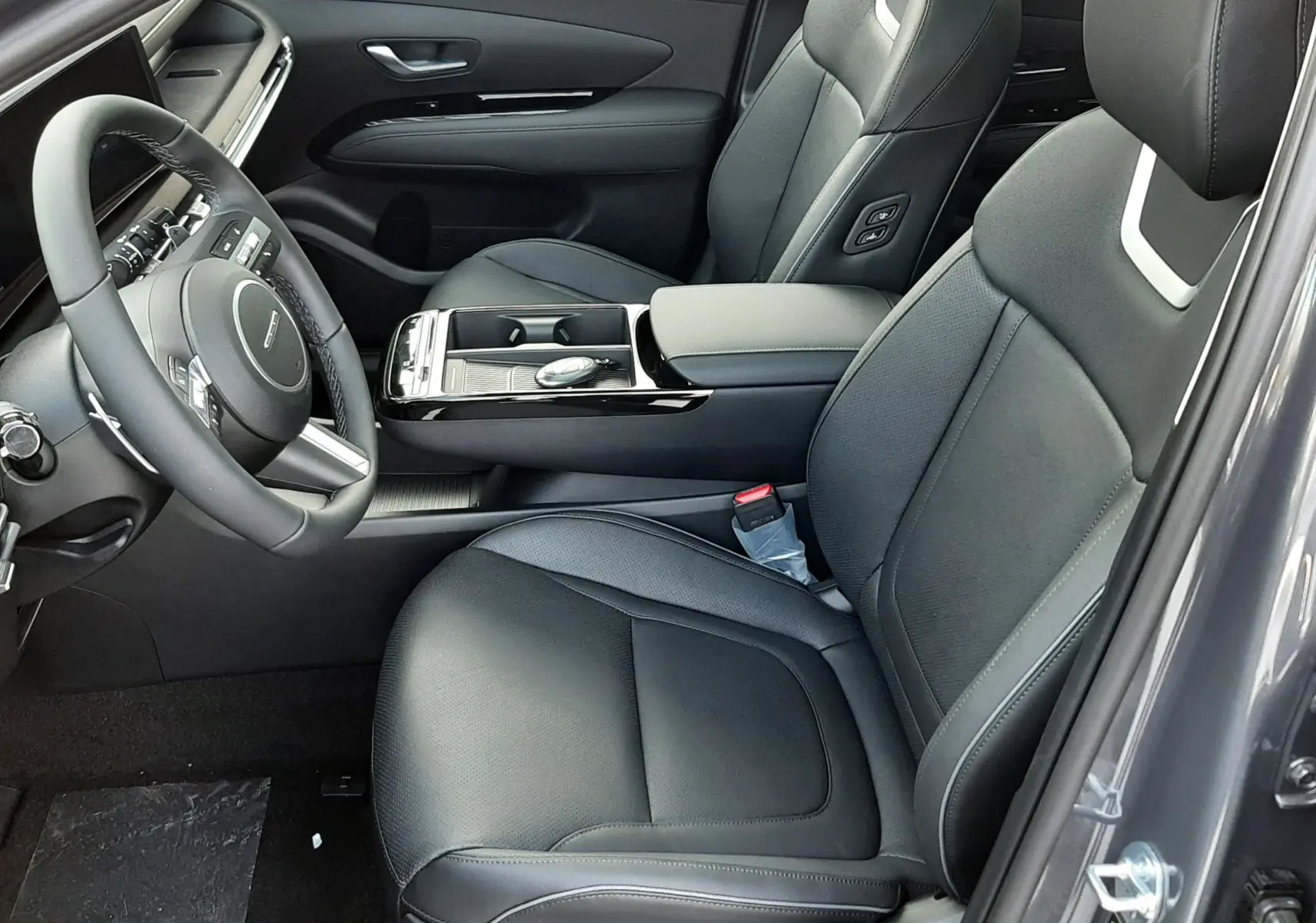 Intérieur côté conducteur du Hyundai Tucson 2025 gris, sièges cuir noirs avec commandes électriques et console centrale moderne.