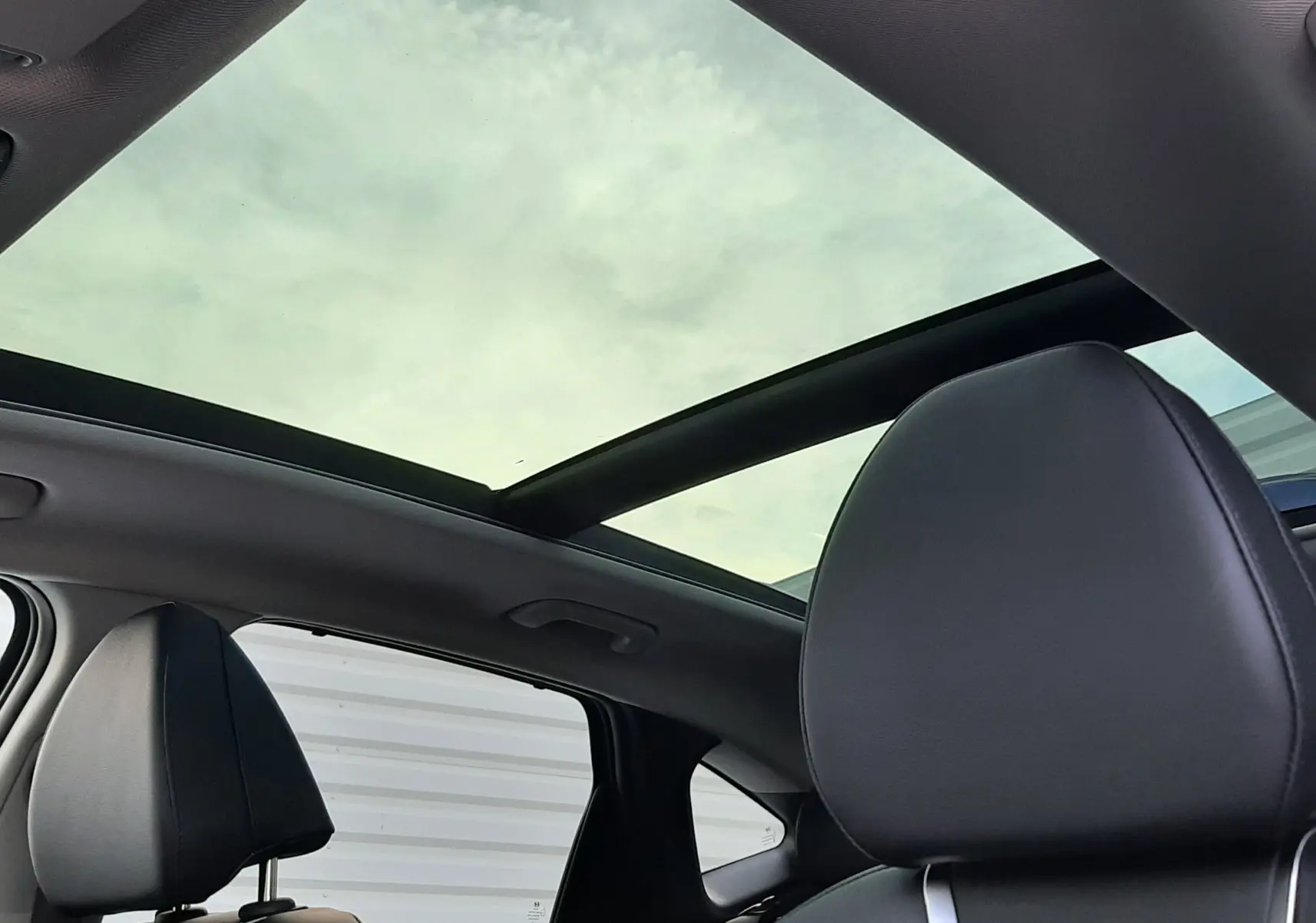 Vue intérieure sur les sièges avant en cuir noir et le toit panoramique ouvrant du Hyundai Tucson 2025 gris Ecotronic.