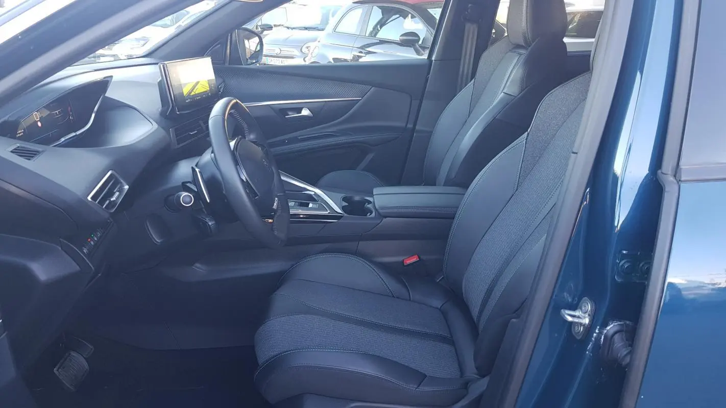 Intérieur côté conducteur du Peugeot 5008 bleu 2024, avec sièges tissu-cuir, écran tactile et volant cuir visible.