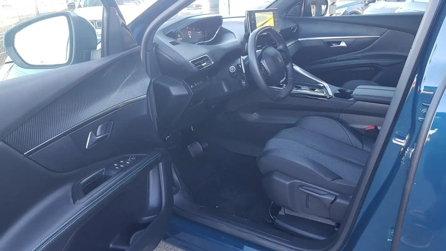 Vue intérieure côté conducteur du Peugeot 5008 bleu 2024, avec volant cuir, écran tactile et sièges réglables.