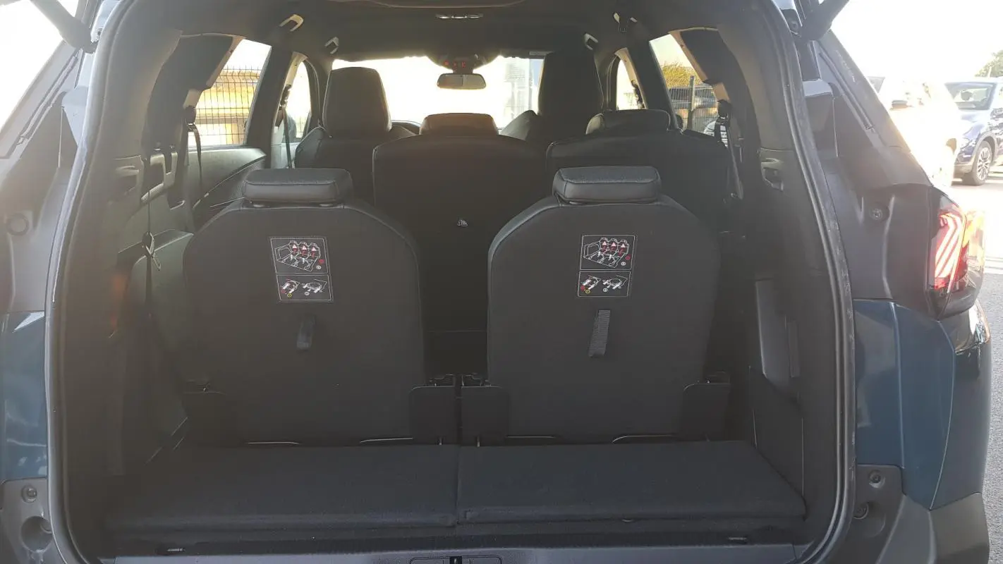 Vue arrière du coffre ouvert d’un Peugeot 5008 bleu 2024, montrant les sièges arrière rabattus et la banquette centrale.