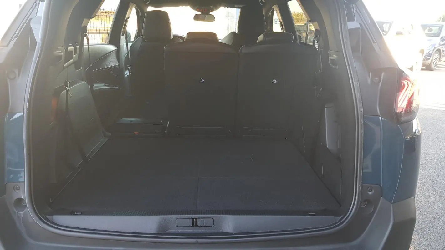 Coffre ouvert vu de l'arrière d'un Peugeot 5008 bleu 2024, montrant l'espace de chargement et les sièges arrière rabattus.