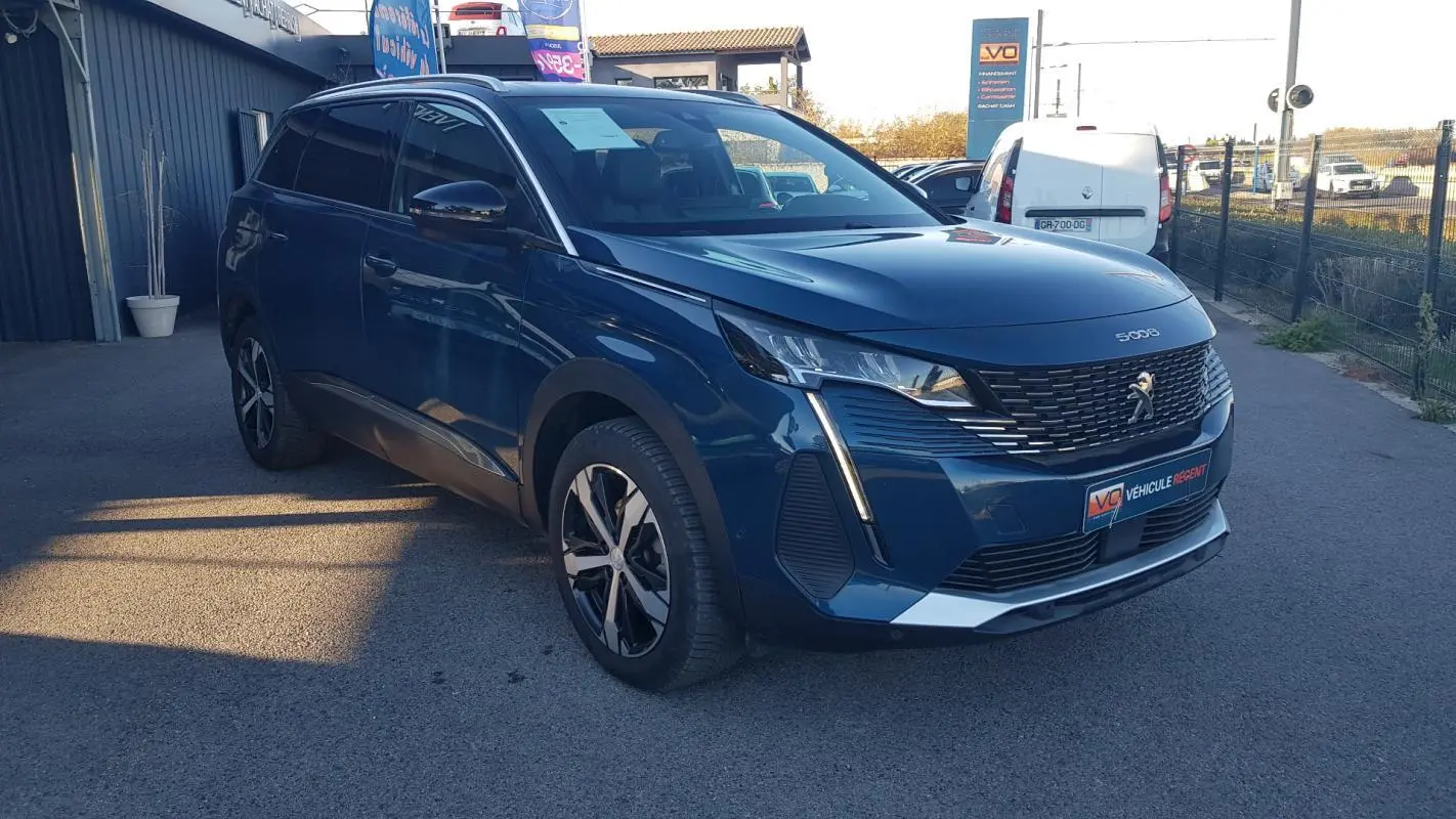 Peugeot 5008 bleu en 3/4 avant droit, avec barres de toit, jantes alliage 18 pouces et rétroviseurs dégivrants.