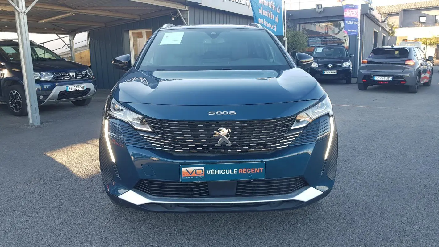 Vue frontale d’un Peugeot 5008 bleu 2024 avec calandre noire, feux LED allumés et plaque « Véhicule récent ».
