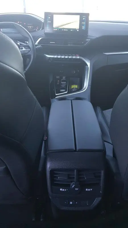 Intérieur du Peugeot 5008 2024 en vue centrale arrière, avec écran tactile, volant cuir et accoudoir central noir.