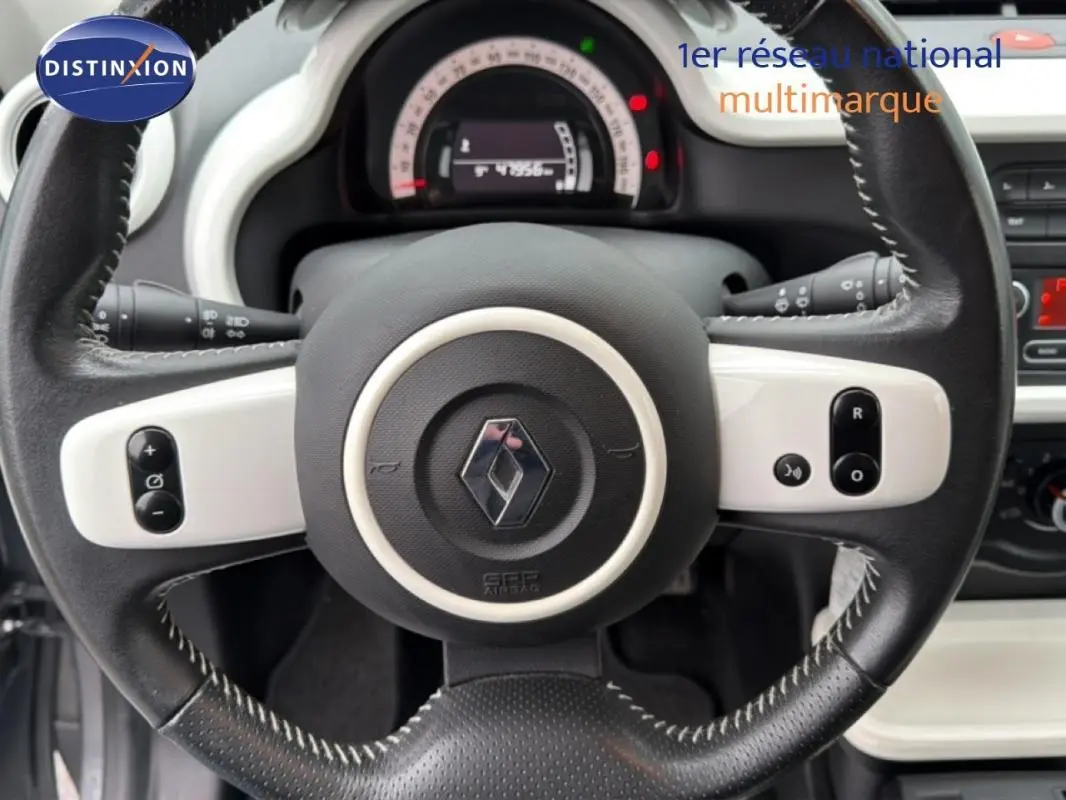 Vue rapprochée du volant cuir noir et blanc de la Renault Twingo III gris foncé, avec commandes intégrées visibles.