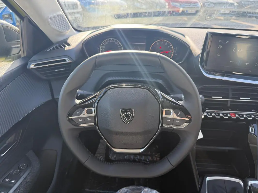 Vue intérieure centrée sur le volant compact de la Peugeot 208 2025 avec tableau de bord et écran tactile visibles.