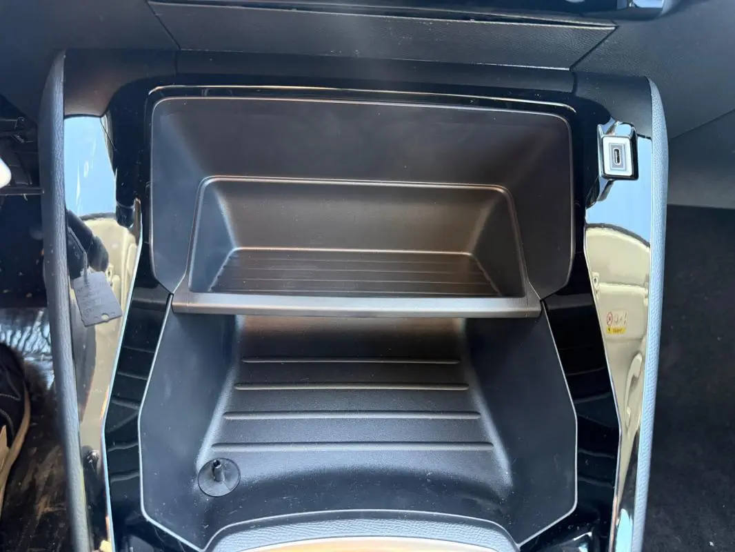 Gros plan sur le rangement central noir brillant de la Peugeot 208 jaune 2025, avec prise USB visible.