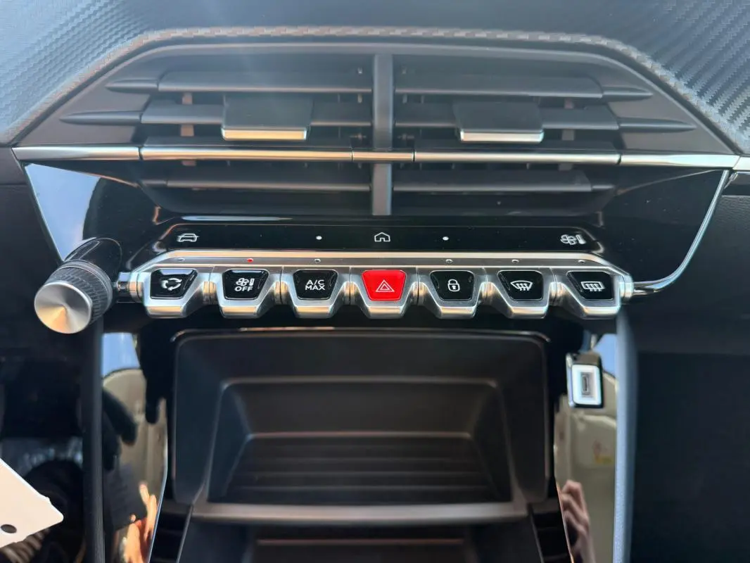 Gros plan sur la console centrale de la Peugeot 208 jaune 2025, montrant les commandes climatisation et boutons fonctionnels.