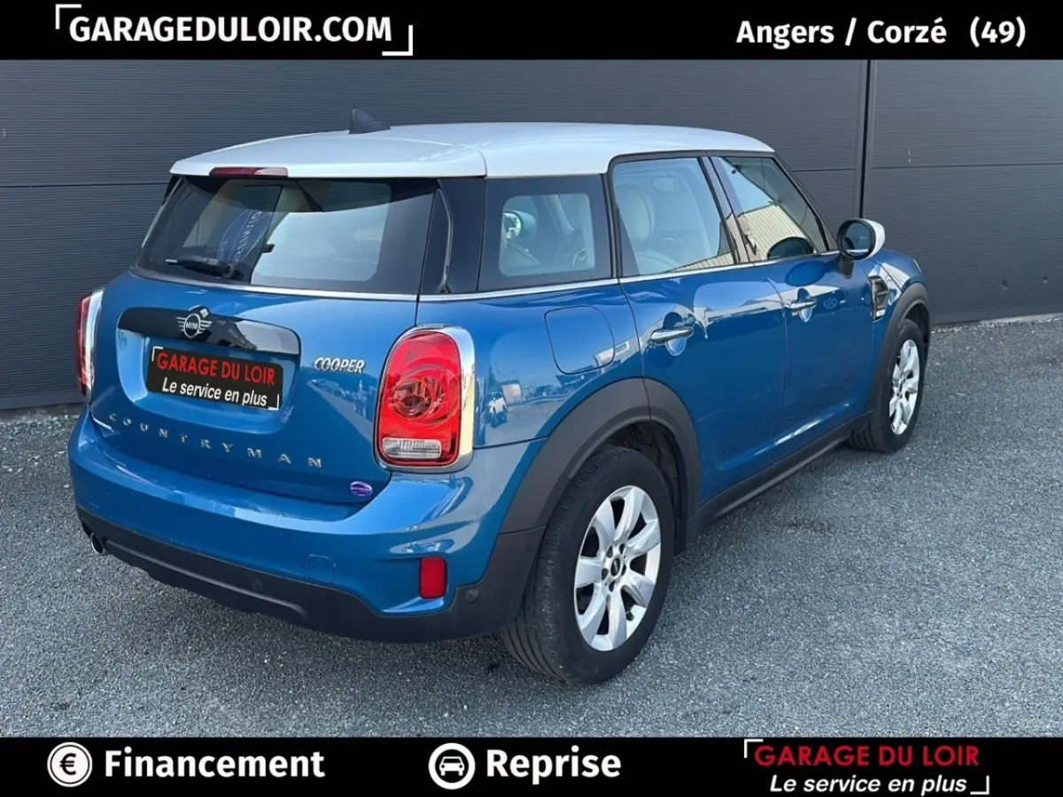 Vue 3/4 arrière droite d'une MINI Countryman Cooper bleu avec toit blanc, feux arrière distinctifs et jantes argentées.
