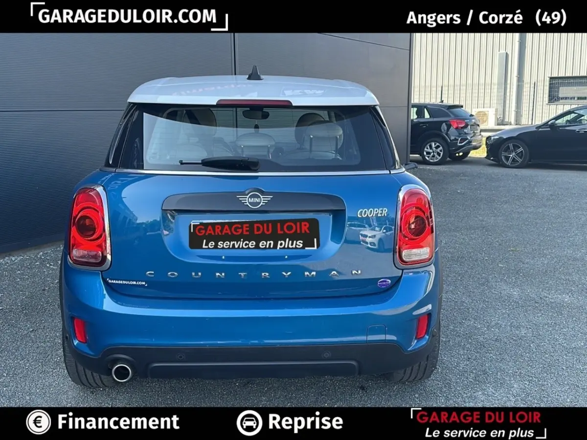 Vue arrière d'une MINI Countryman Cooper bleu avec toit blanc, feux rouges et double sortie d'échappement visible.