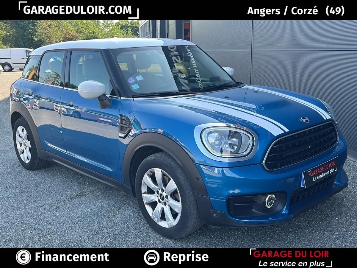 Vue 3/4 avant d'une MINI Countryman Cooper Exquisite bleu avec toit blanc et bandes blanches sur le capot, garée sur un sol gravillonné.