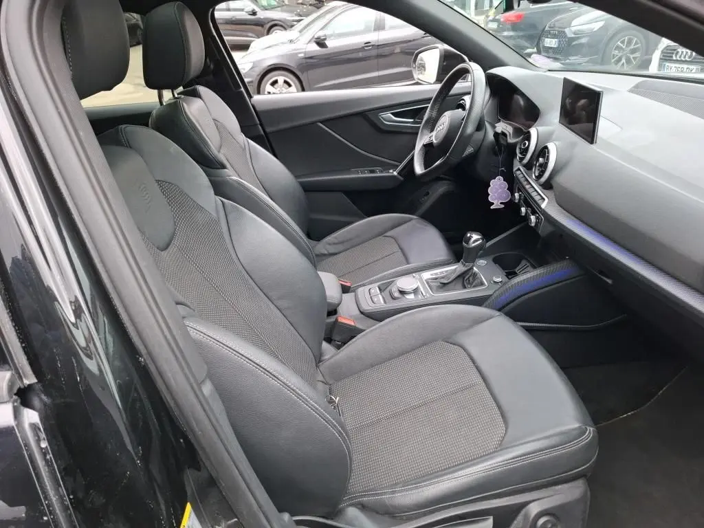 Vue intérieure côté conducteur de l'Audi Q2 noir 2023, sièges sport en cuir avec logo S embossé sur appuie-têtes.