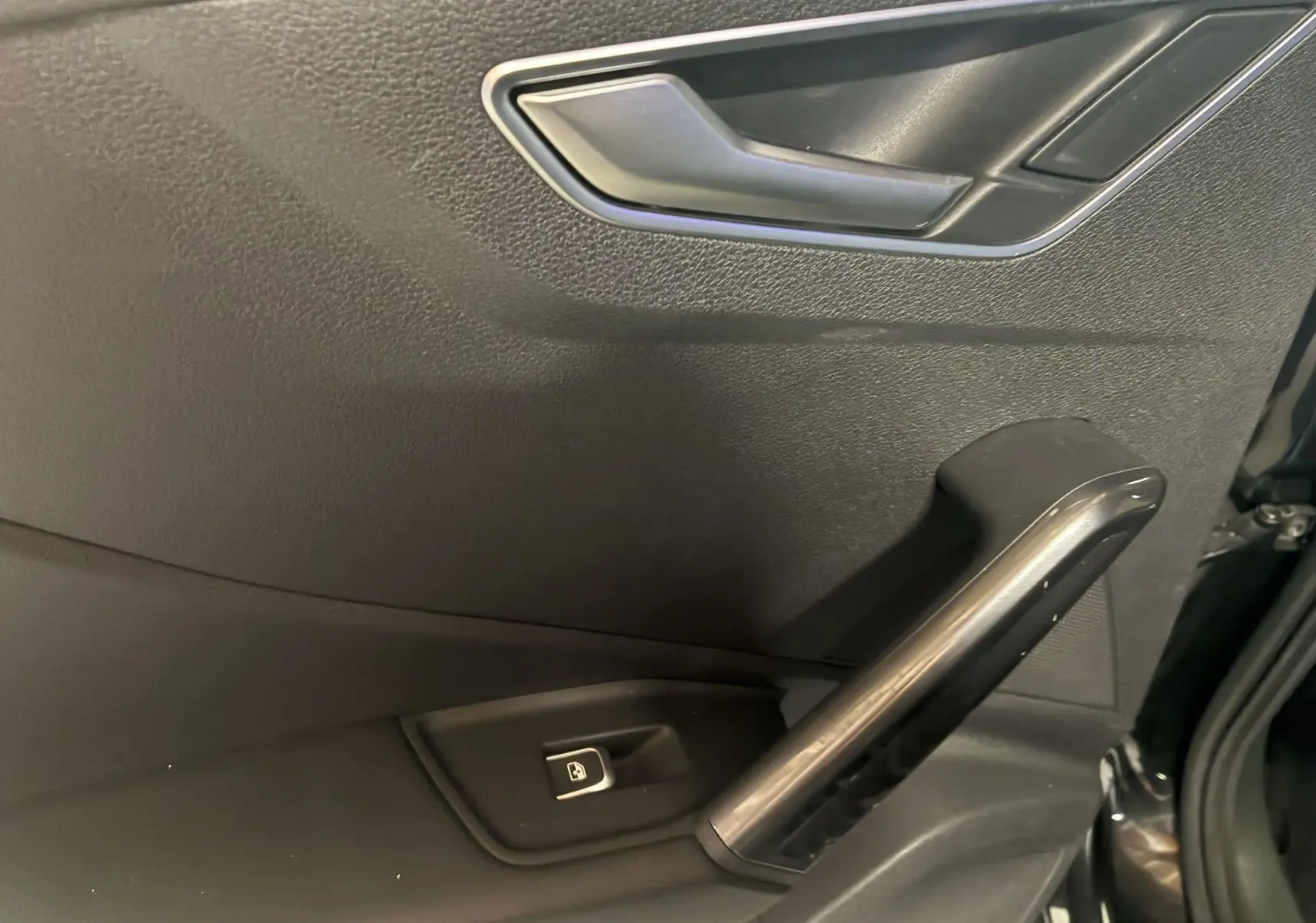 Détail de la porte intérieure côté conducteur noire de l'Audi Q2 2023 avec poignée et bouton de verrouillage électrique.