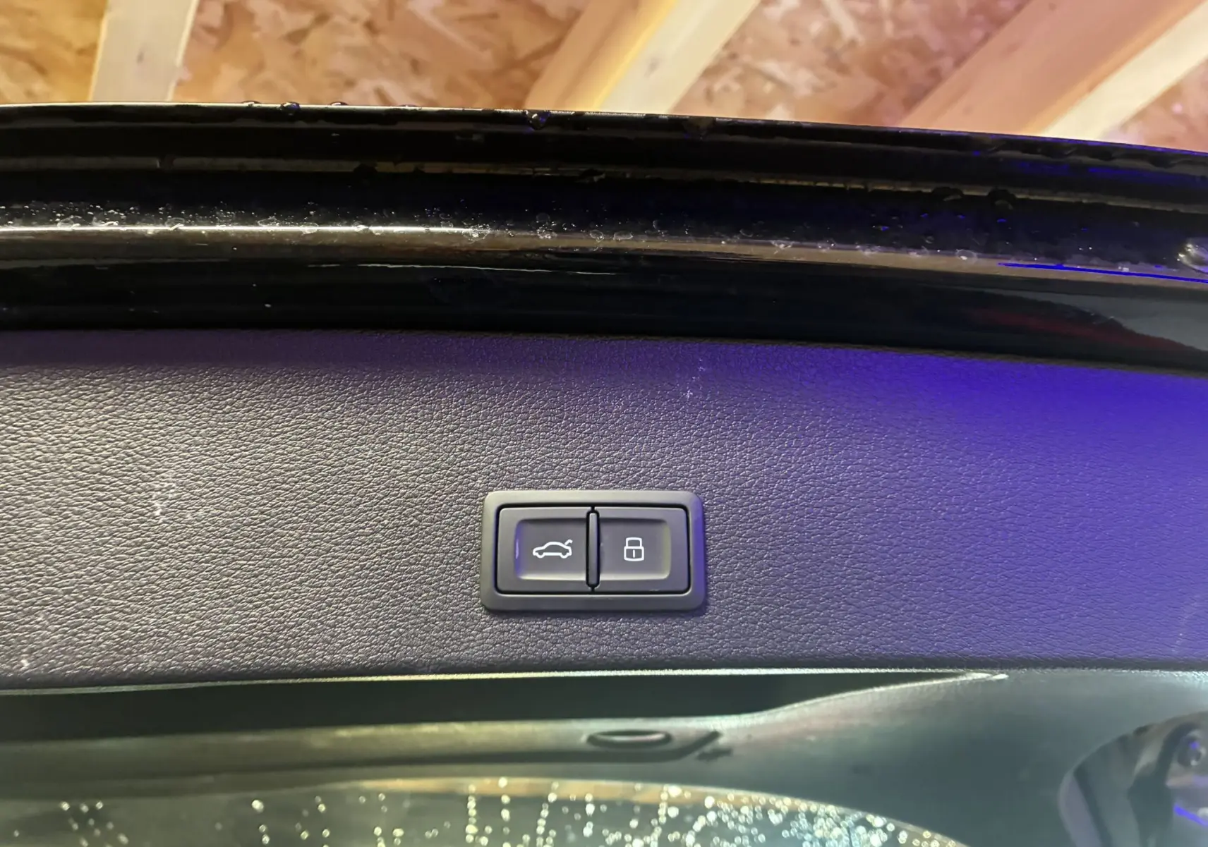 Gros plan sur les boutons d'ouverture et de verrouillage du coffre, intérieur noir du hayon d'un Audi Q2 noir.