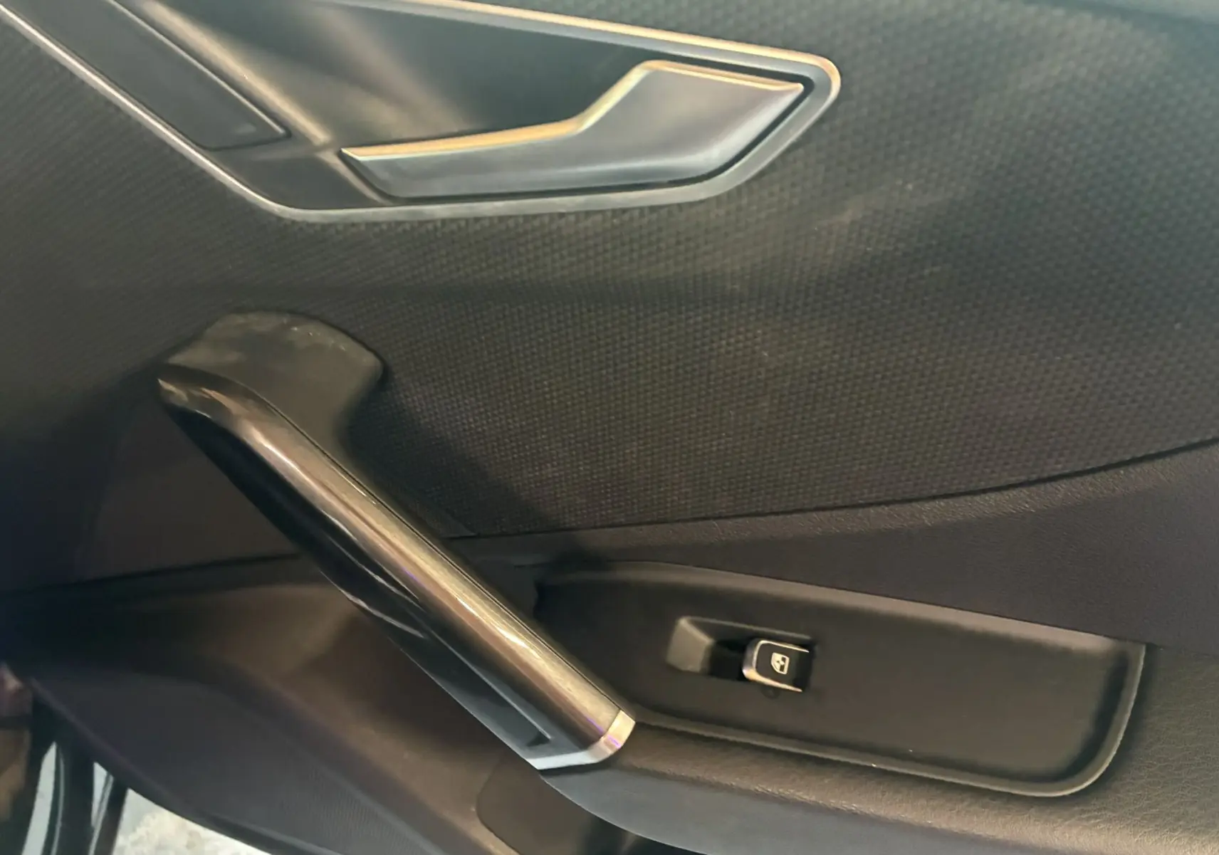 Détail de la porte intérieure côté conducteur de l'Audi Q2 noire, avec poignée et bouton de commande de vitre électrique.