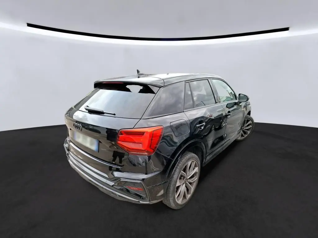 Audi Q2 noir en 3/4 avant droit, avec calandre noire et jantes alliage, stationné dans un garage moderne.