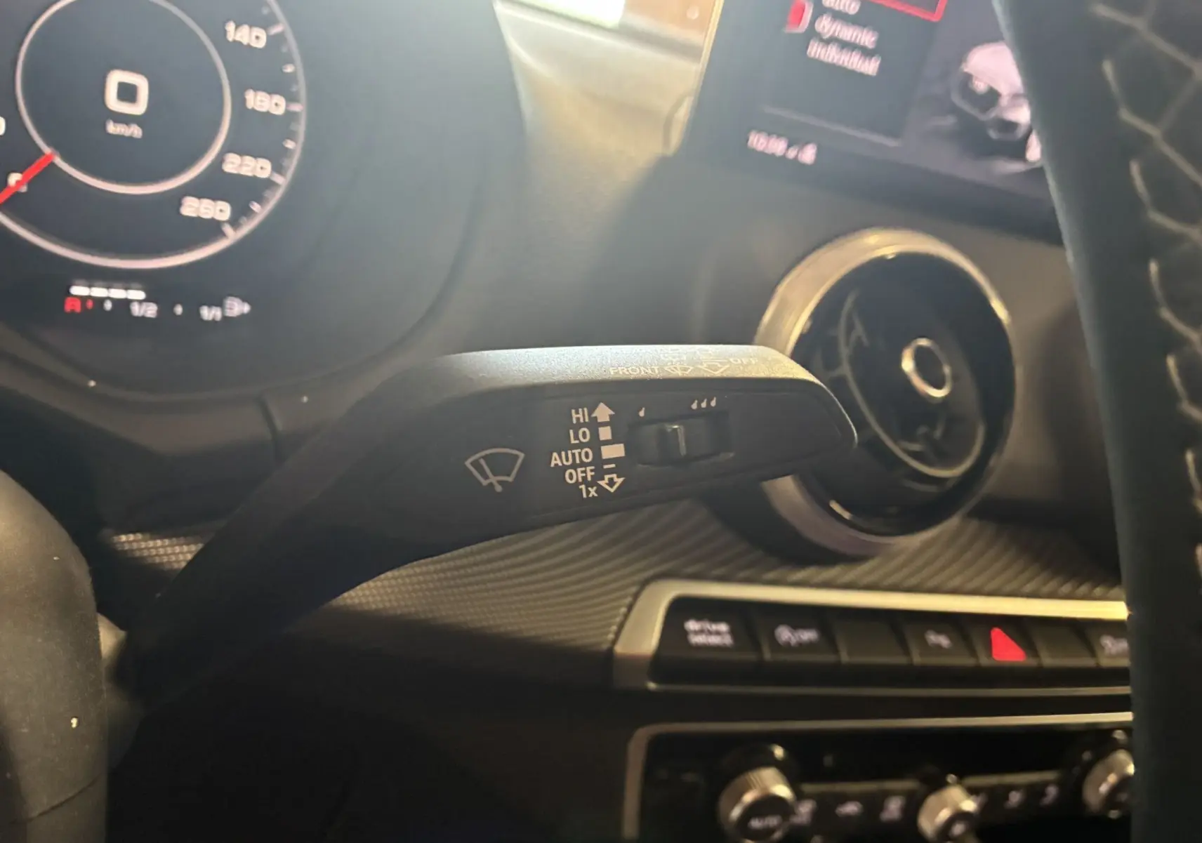Gros plan sur la commande d’essuie-glace à gauche du volant d’un Audi Q2 noir, avec tableau de bord et aérateur circulaire visibles.