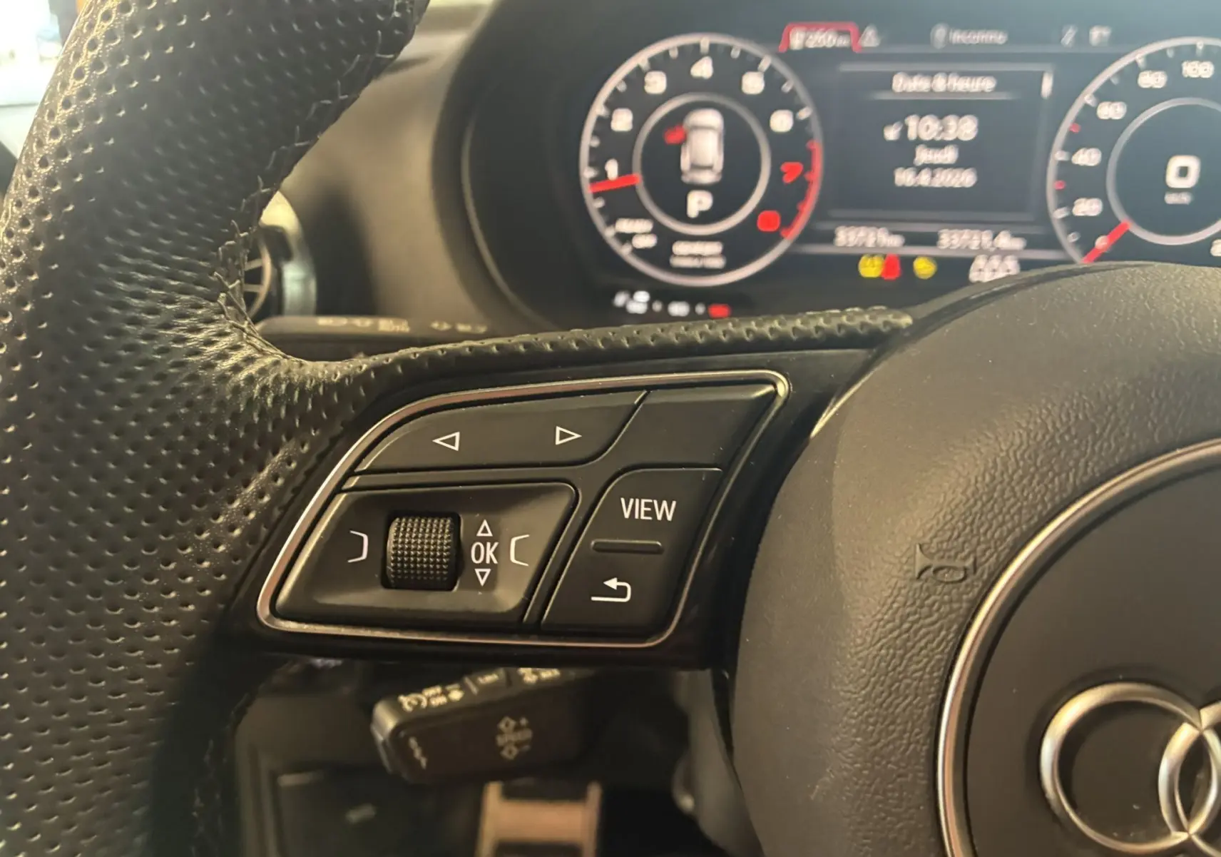 Gros plan sur les commandes gauche du volant cuir perforé noir d’un Audi Q2 2023 avec tableau de bord numérique en arrière-plan.