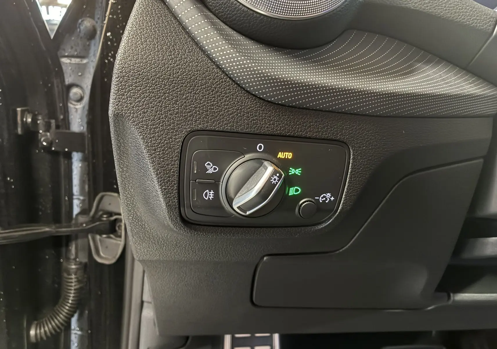 Gros plan sur le panneau de commande des phares à gauche du volant dans l’Audi Q2 noir, avec réglage automatique activé.