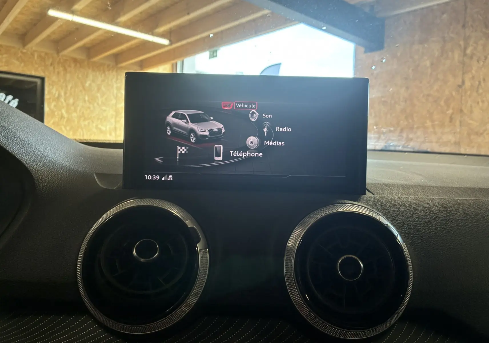 Écran central affichant le menu multimédia avec image d'un Audi Q2 gris, entouré de deux aérateurs ronds noirs.