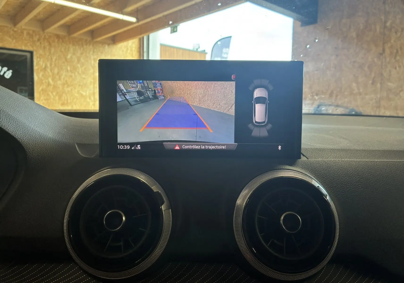 Vue intérieure du tableau de bord de l'Audi Q2 noir 2023, écran de caméra de recul et aérateurs ronds chromés.