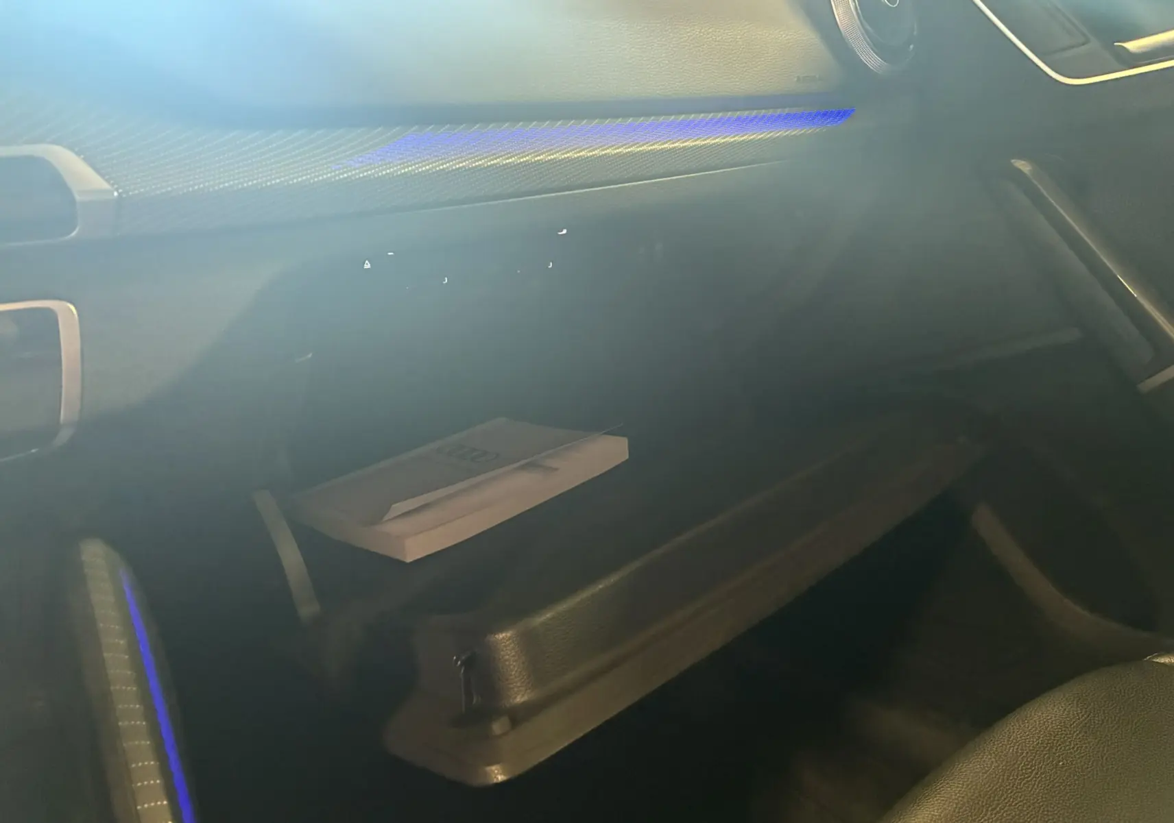 Vue intérieure de la boîte à gants ouverte de l'Audi Q2 2023 avec éclairage d'ambiance bleu et manuel visible.