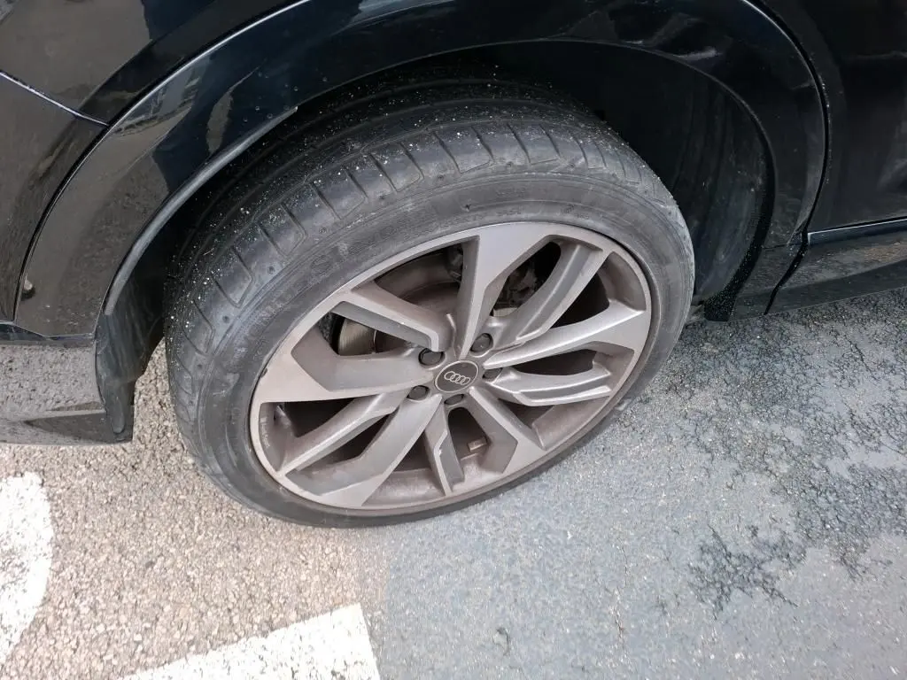 Audi Q2 noir vue de profil côté gauche, jantes alliage distinctives, stationné en intérieur avec mur en bois.