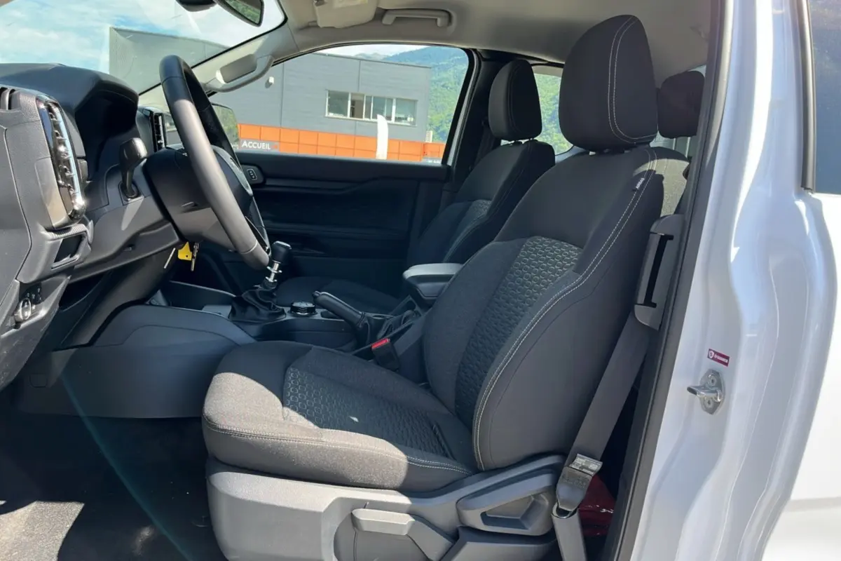 Intérieur du Ford Ranger blanc glacier 2026, vue côté conducteur avec sièges noirs et tableau de bord visible.