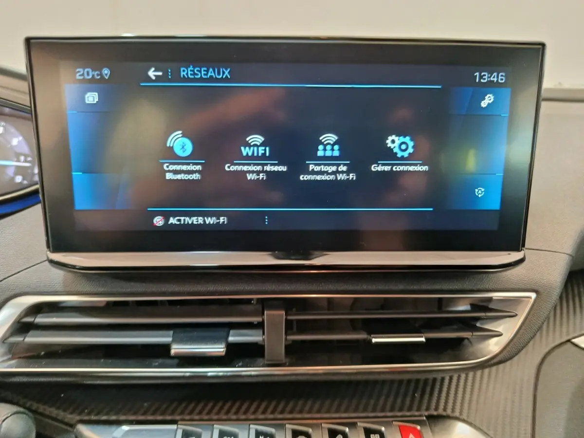 Écran tactile central affichant les options réseau Wi-Fi et Bluetooth, avec aérateurs et tableau de bord noir.