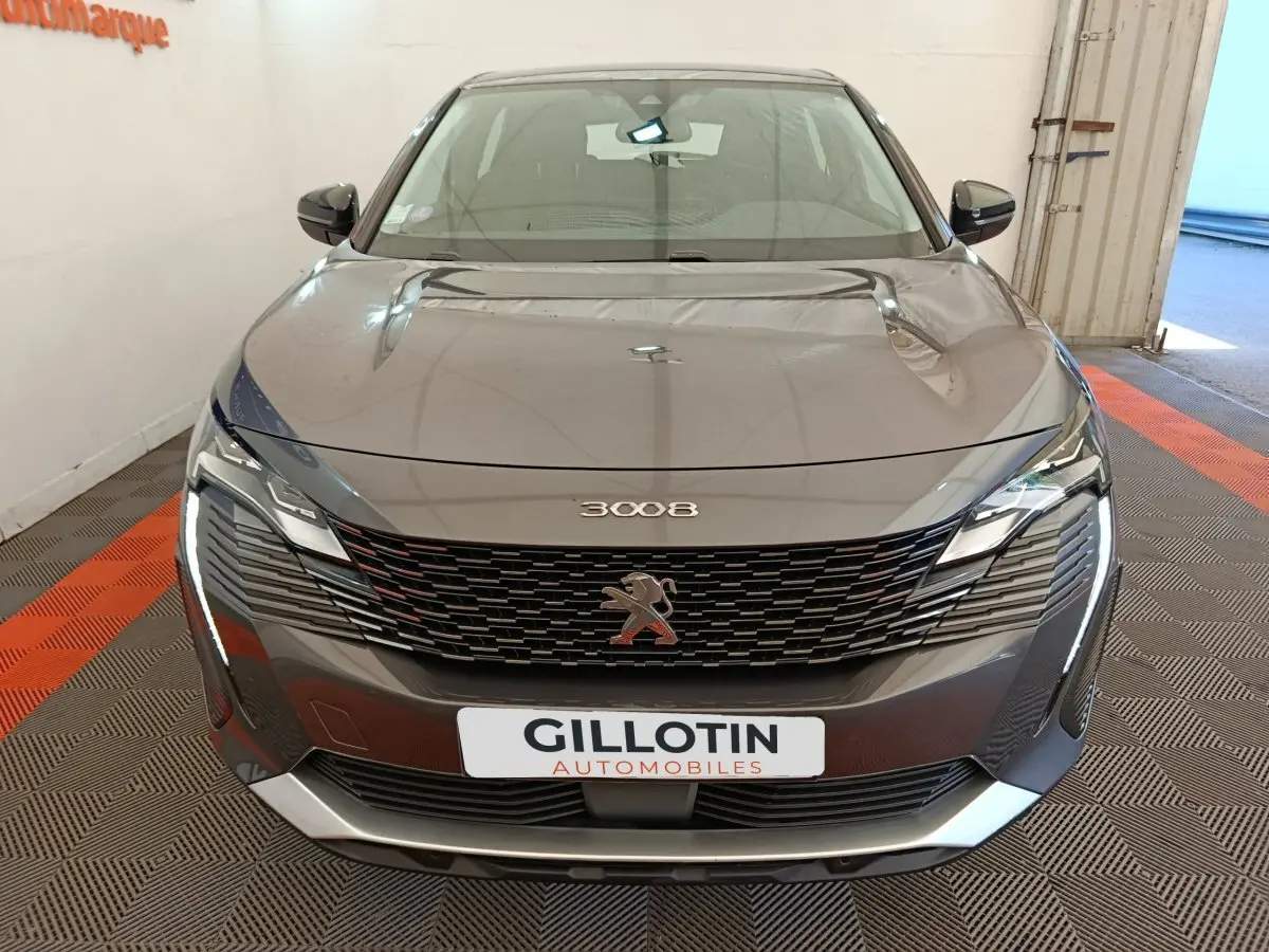 Vue avant d’un Peugeot 3008 gris foncé avec calandre noire et phares LED distinctifs, en intérieur showroom.