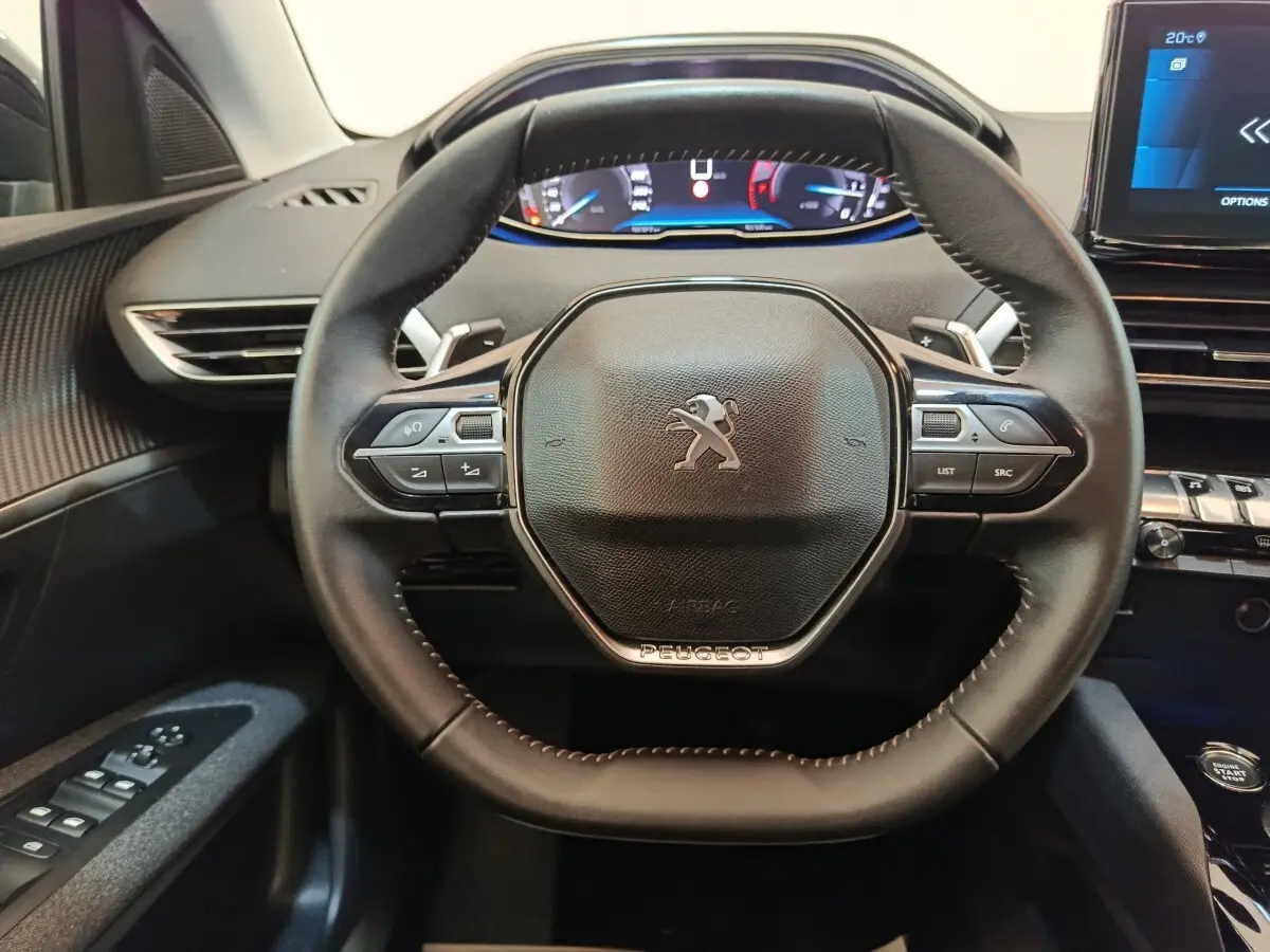Vue rapprochée du volant cuir noir du Peugeot 3008 2022 avec commandes multifonctions et affichage digital en arrière-plan.