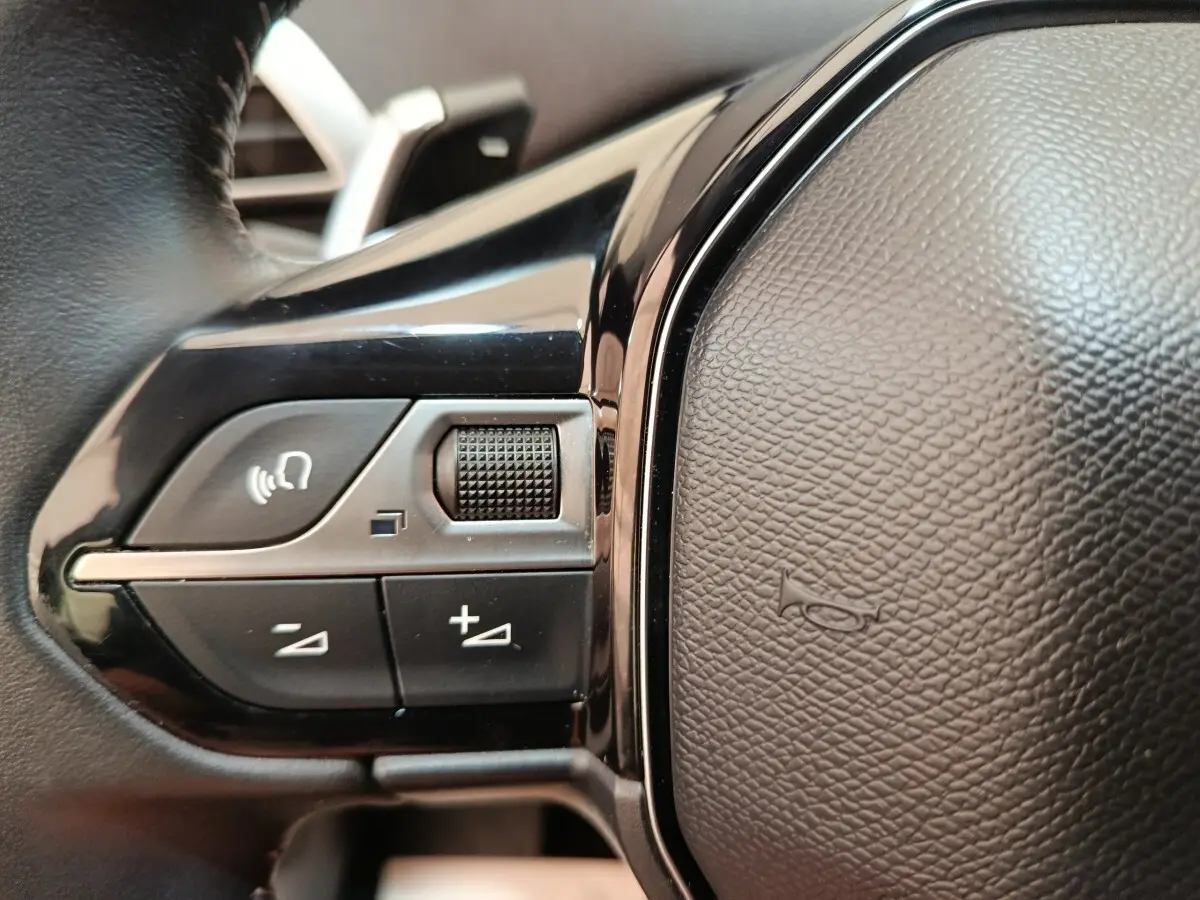 Gros plan sur les commandes de volume et de reconnaissance vocale sur le volant cuir noir du Peugeot 3008 gris foncé.