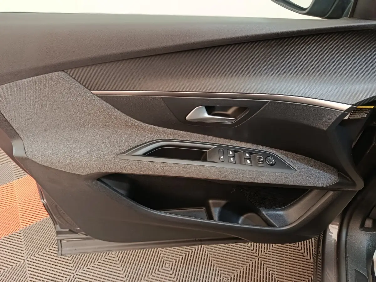 Vue intérieure côté gauche de la porte avant d’un Peugeot 3008 gris foncé avec commandes électriques des vitres et poignée argentée.