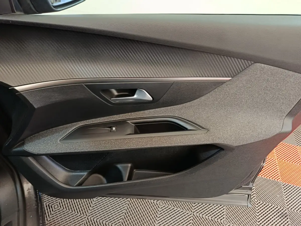 Vue intérieure côté gauche de la porte avant d'un Peugeot 3008 gris foncé avec habillage tissu et plastique noir.