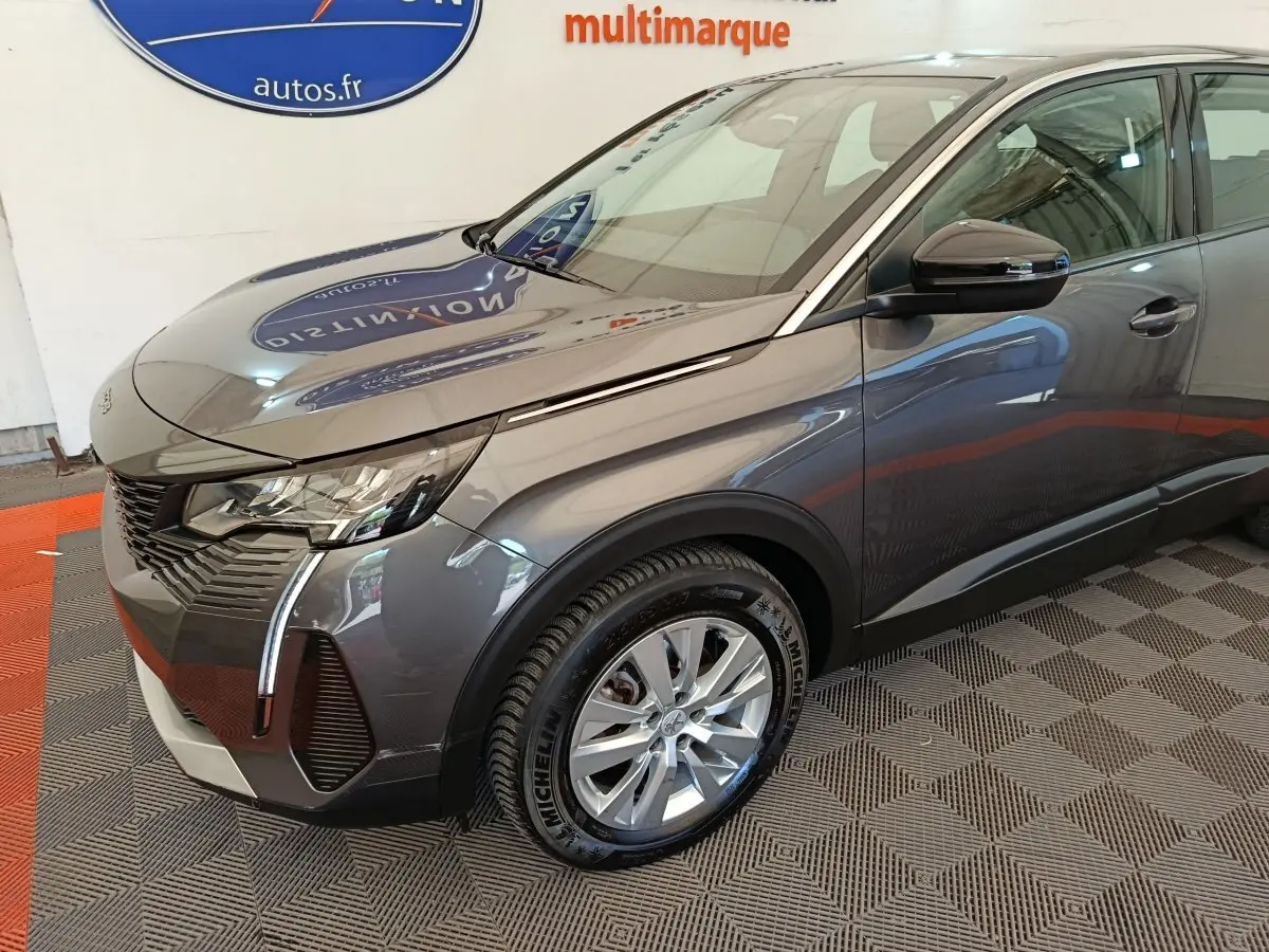 Vue 3/4 avant droit d'un Peugeot 3008 gris foncé avec phares LED et jantes alliage visibles en intérieur showroom.